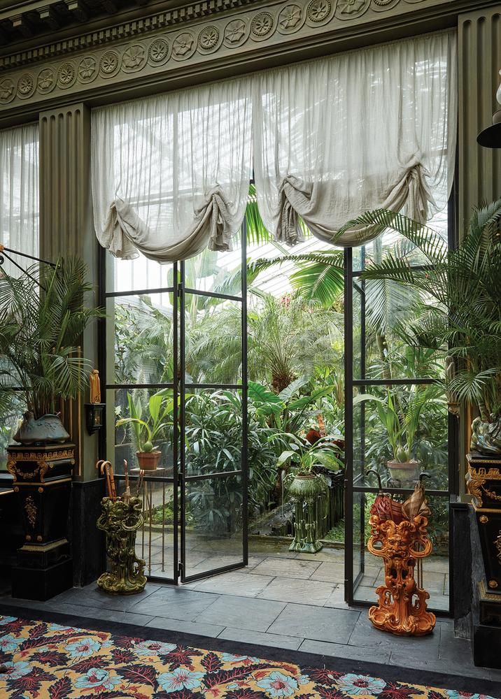 the inside of a building with lots of plants and decorations in front of large windows