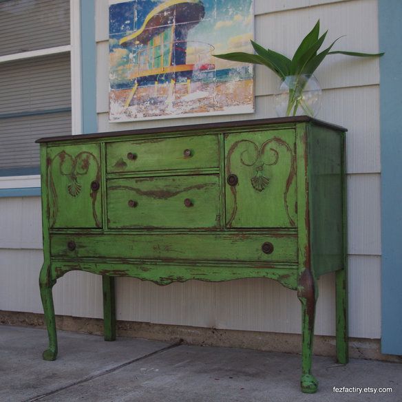 an old dresser painted green in front of a house with a painting on the wall