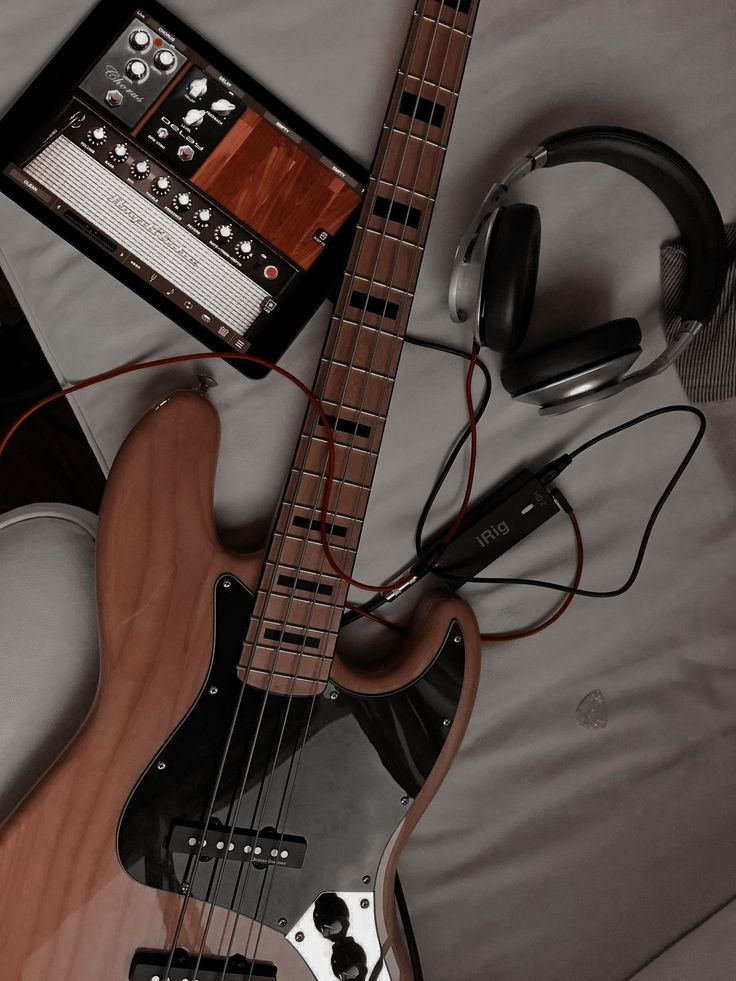 an electric guitar and headphones are laying on a bed next to a tablet computer