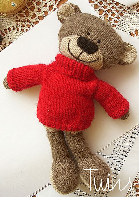 a knitted teddy bear in a red sweater laying on top of a piece of paper