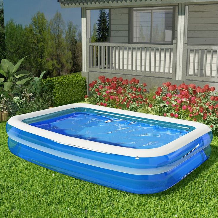 an inflatable swimming pool on the lawn with flowers around it and a house behind