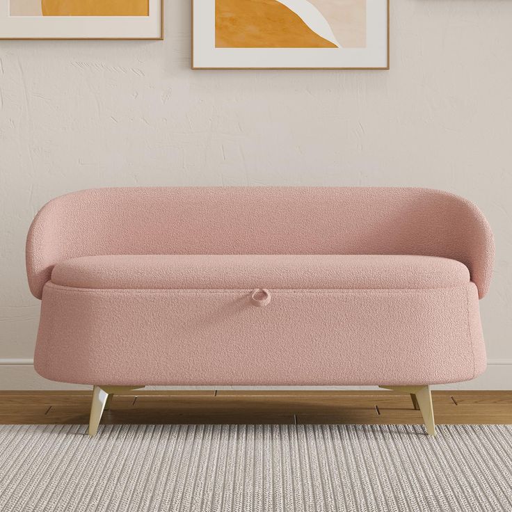 a pink couch sitting on top of a wooden floor next to two framed pictures above it