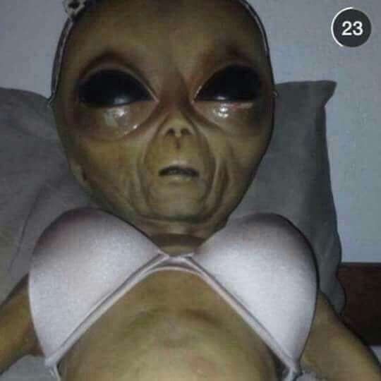 an alien doll wearing a white bra laying on top of a bed next to a pillow