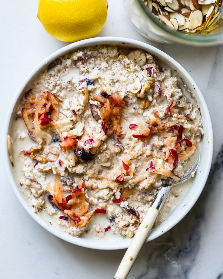 a bowl of oatmeal with fruit and nuts next to a lemon on the side