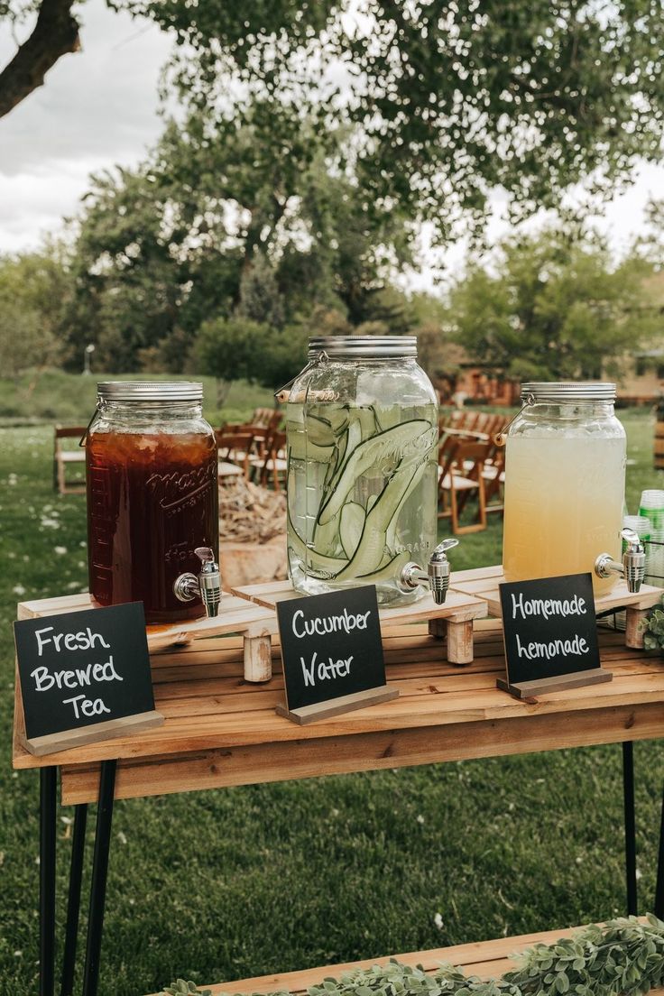 mason jars filled with liquid sit on a wooden table in the middle of a field