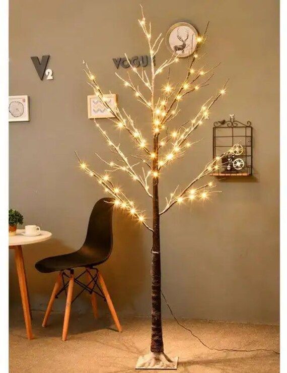 a small tree with lights on it and a chair in the corner next to it