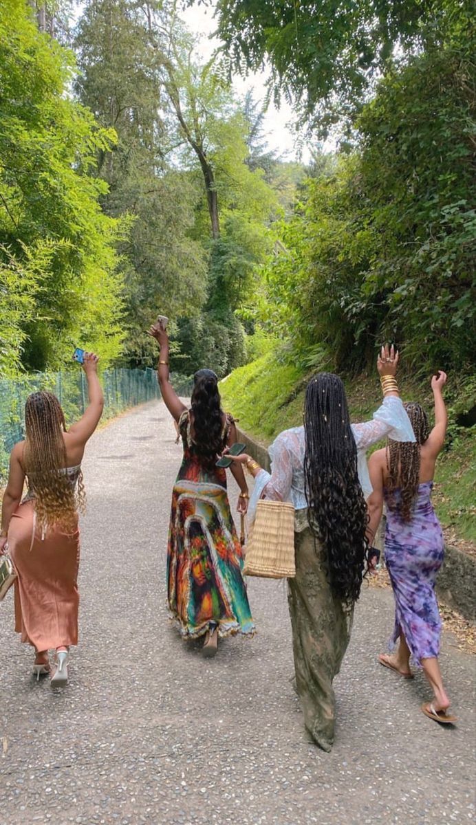 three women walking down a road with their arms in the air and one woman holding her hand up