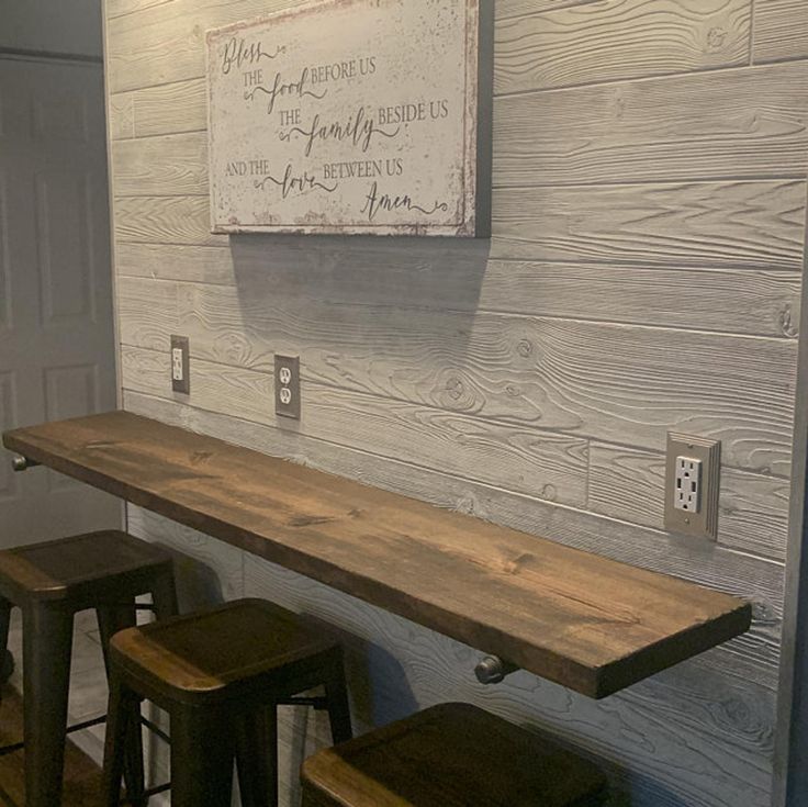 three wooden stools sitting in front of a wall with a sign hanging on it