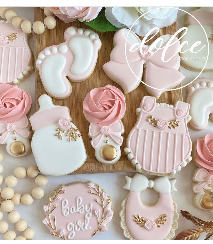 baby shower cookies with pink icing and gold accents on a cutting board next to flowers