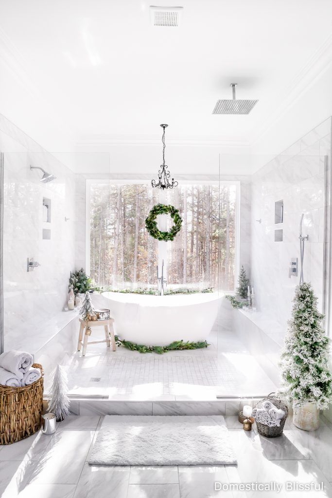 a white bathroom with a wreath hanging from the ceiling next to a bathtub in front of a window