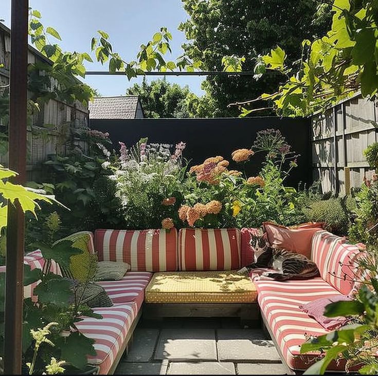 a cat sitting on a striped couch in the middle of a garden with lots of flowers