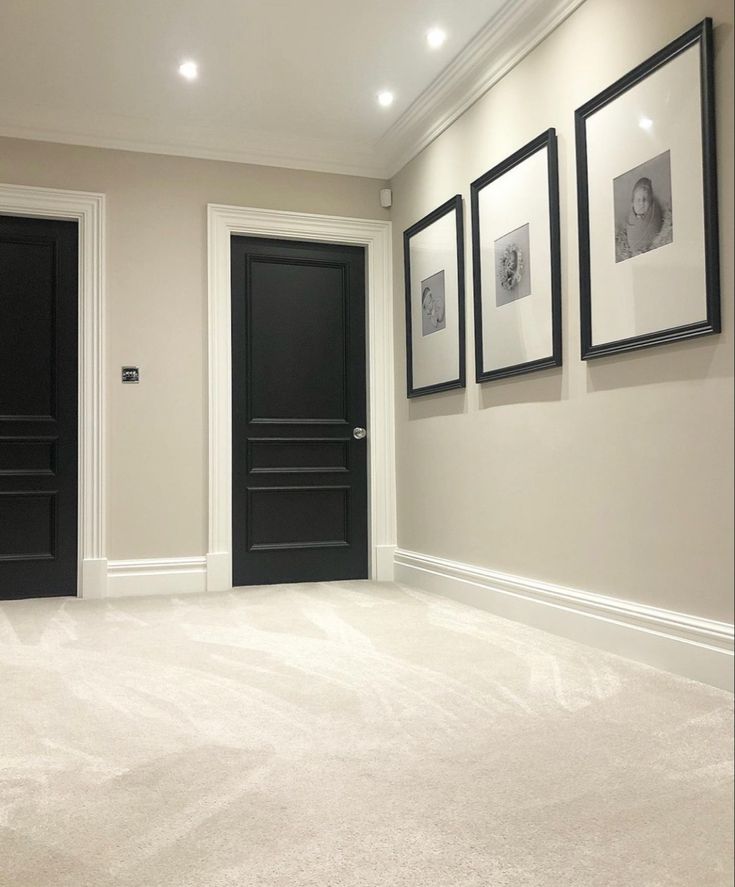 an empty room with three black doors and pictures on the wall above it, along with carpeted flooring