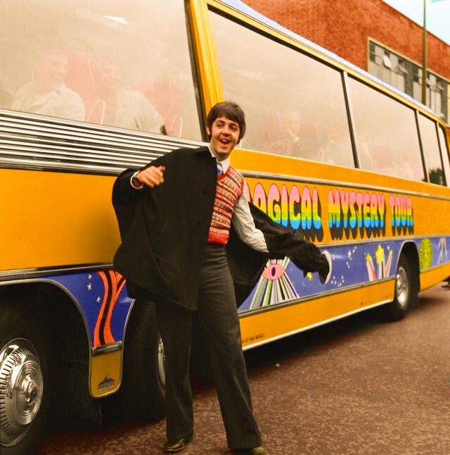 a man standing in front of a yellow bus on the street with his arms out