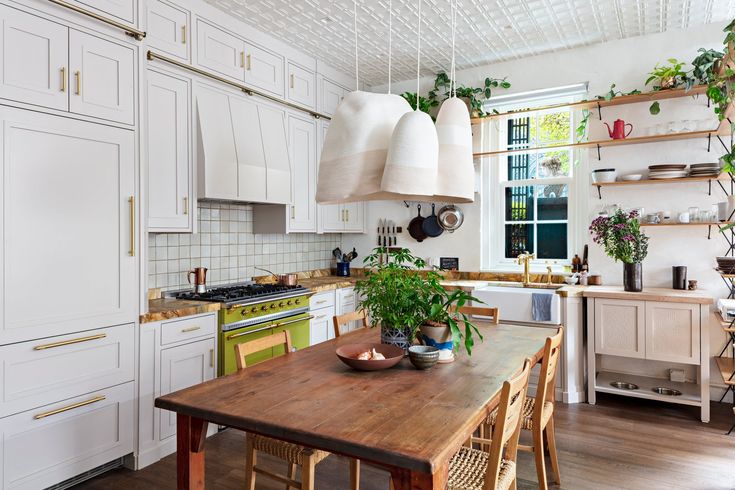 a kitchen filled with lots of white cabinets and wooden table topped with potted plants