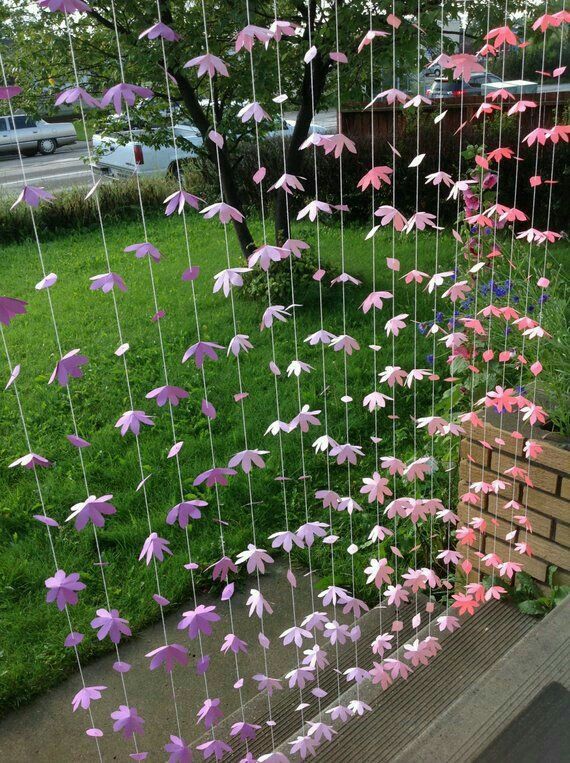 some pink and purple paper cranes hanging from the side of a fence in front of a green lawn