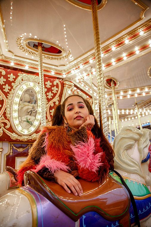 a woman sitting on top of a merry go round horse talking on a cell phone