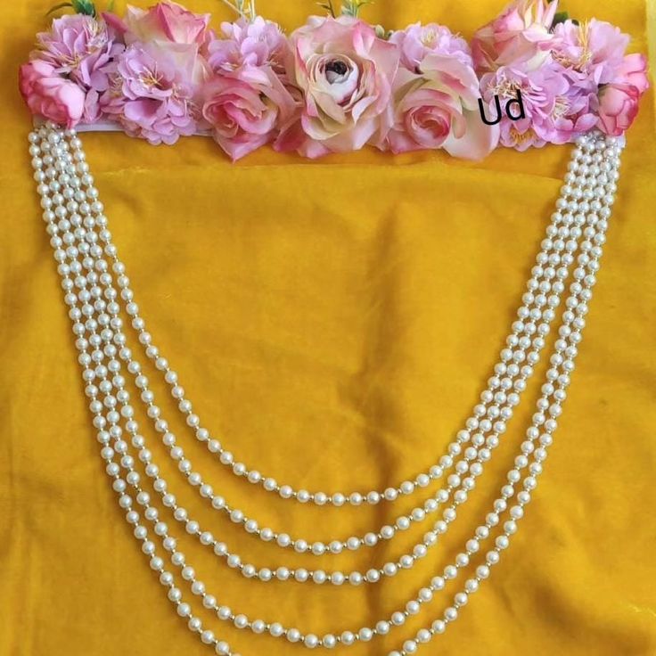 three strand pearl necklace with pink flowers on yellow clothed fabric, ready to be worn