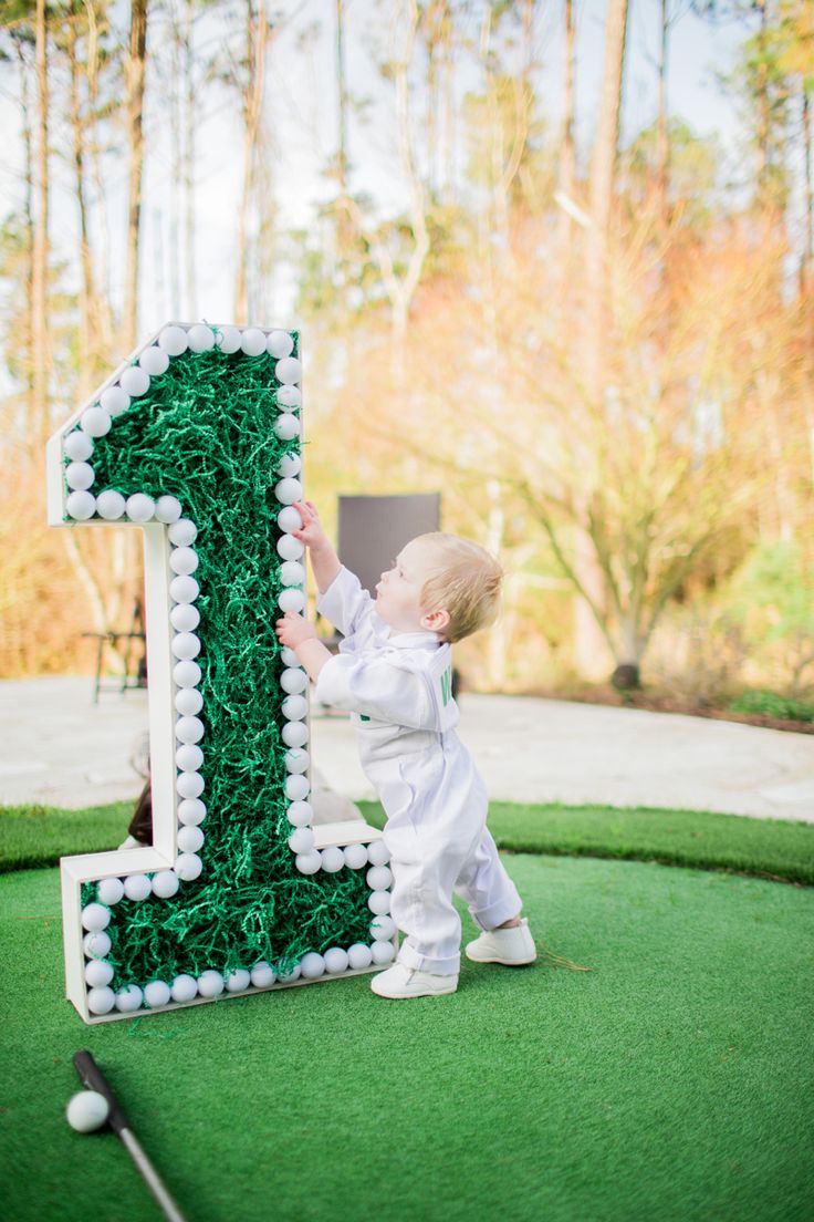 a little boy standing next to a giant number one cake on top of a green field