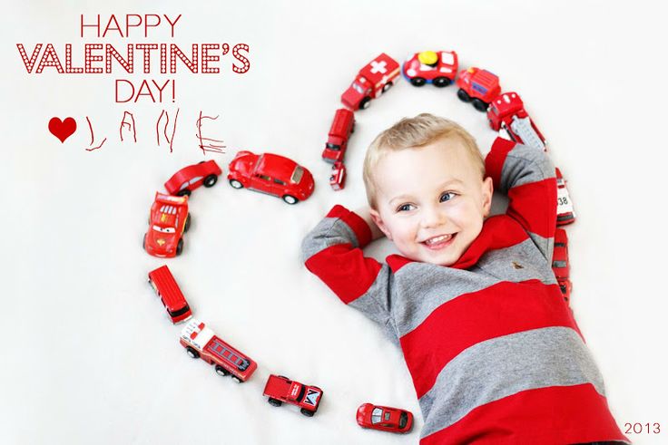 a young boy laying on top of a pile of toy cars next to a happy valentine's day message