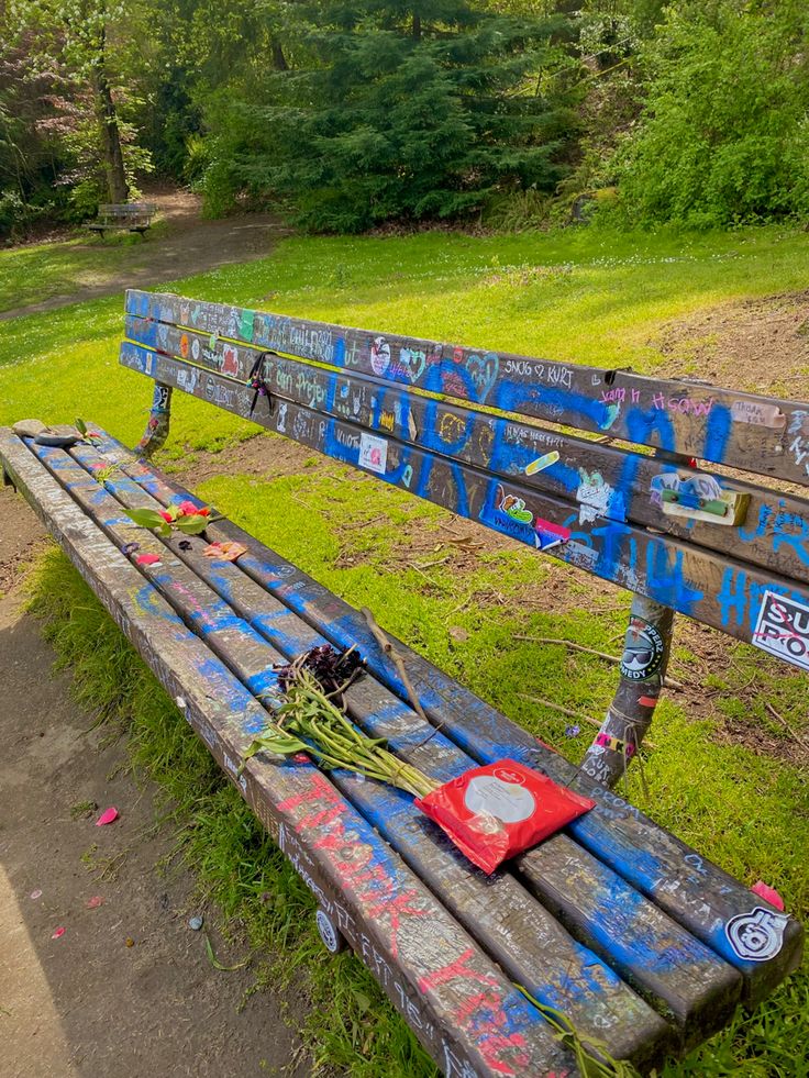 a wooden bench covered in graffiti sitting on top of a lush green park field next to a forest