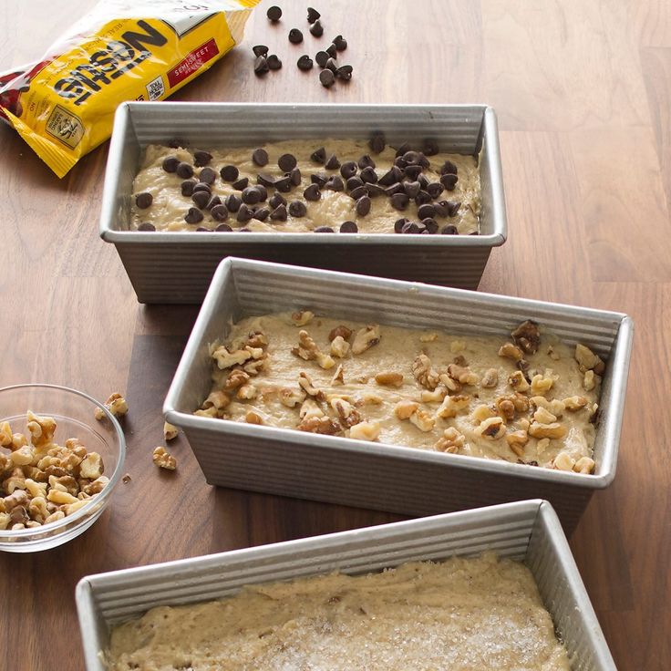 three pans filled with food sitting on top of a wooden table next to a bag of chips