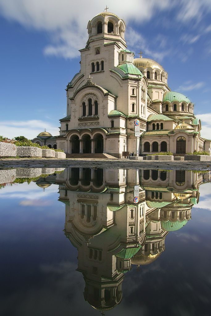 an old building with a green roof is reflected in the still water on a sunny day