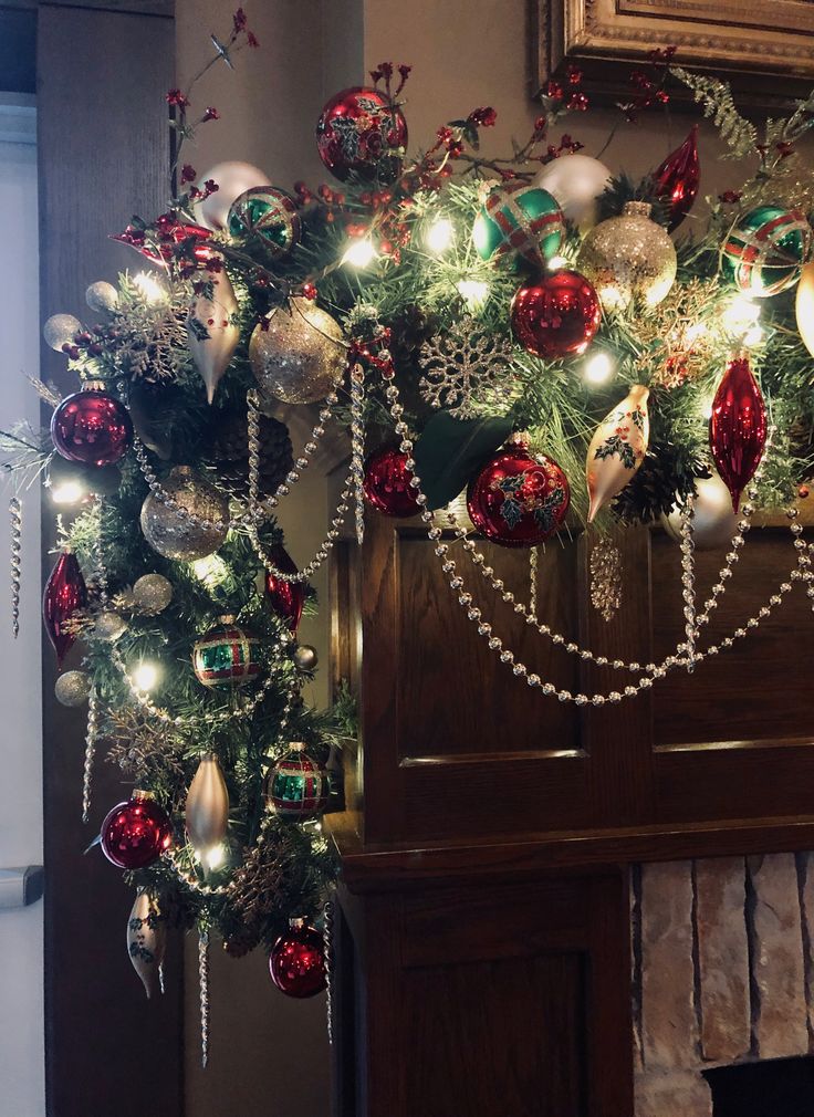 a christmas tree decorated with ornaments and lights in front of a fireplace mantel or mantle