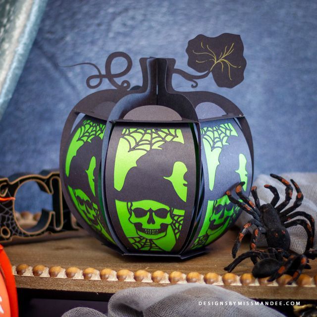 a green and black decorated pumpkin sitting on top of a table next to a spider