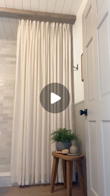 a white curtain hanging from the side of a wall next to a small table with a potted plant on it