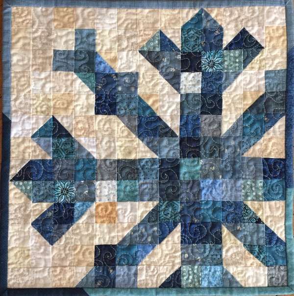 a blue and white quilted wall hanging with an arrow design on the center piece