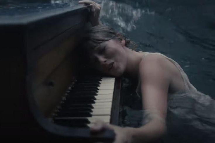 a man laying on top of a piano in the water with his head resting on it