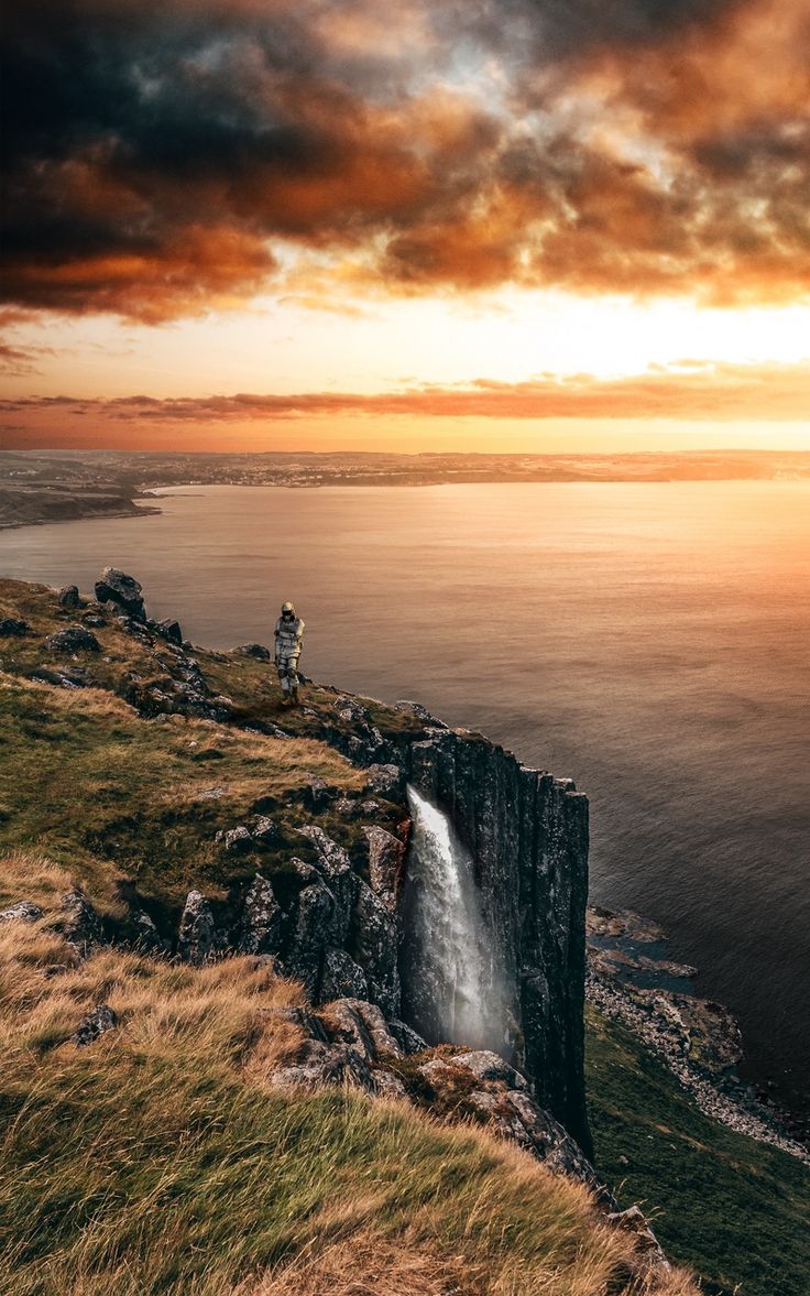 an image of a waterfall on the side of a cliff at sunset or sunrise with clouds in the sky