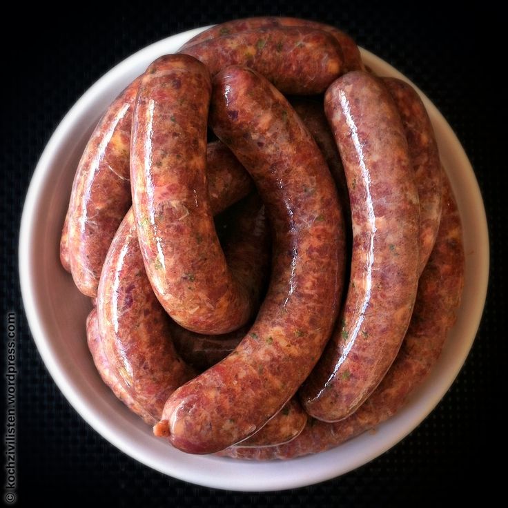 a white bowl filled with sausages on top of a black tableclothed surface