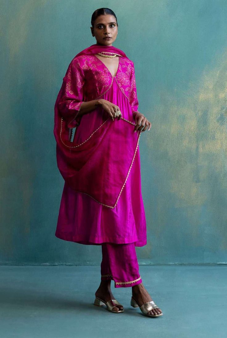 Editor's Note A Fusion Of Western And Indian Silhouette. This V-neck Gather Kurta Is Delicately Crafted In Hand Woven Silk With Gold Floral Hand Print And Gota Highlights. A Sheer Kota Silk Dupatta With Decorative Gold Lace And Silk Pants With This Rich Silk Kurta Makes It A Truly Special One. Color: Pink Fabric: Kurta: Silk, Pant: silk, Dupatta: Kota Silk Care: Dry Clean Only About the Designer Shivani Bhargava defines itself in three words Pure, Natural, and Absolute. The brand concentrates on Sheer Dupatta, Easy Clothing, Pink Anarkali, Pink Cape, Pink Kurta, Silk Pant, Tunics Online, Embroidered Neckline, Kurta With Pants