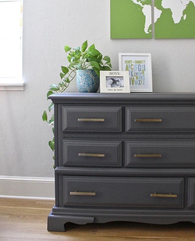 the dresser is painted gray with gold handles and pulls on it's drawers, along with a green plant