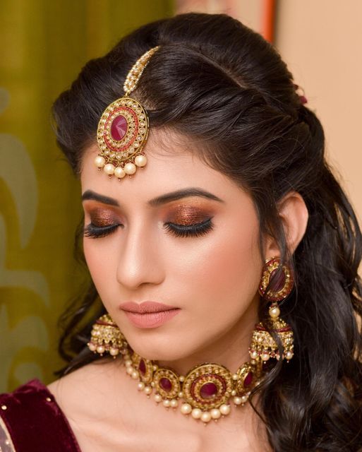 a woman in a red and gold outfit with jewelry on her head, looking at the camera