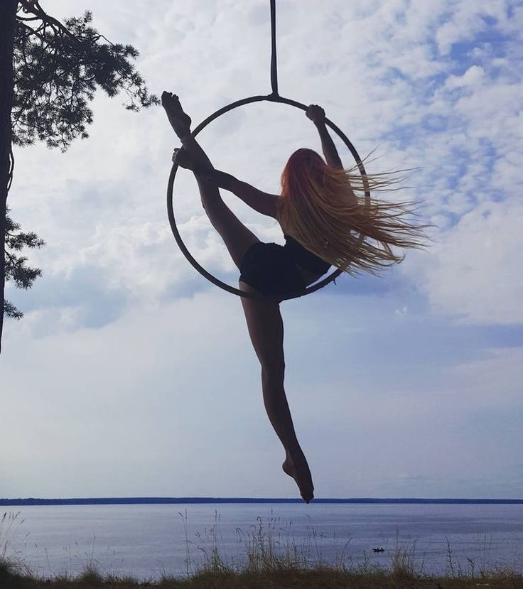 a woman is doing aerial acrobatics on a hoop by the water's edge