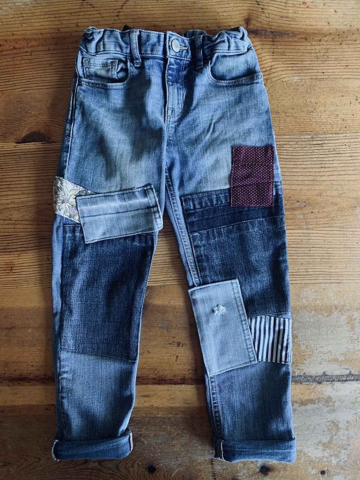 an old pair of jeans with patches on them sitting on top of a wooden floor