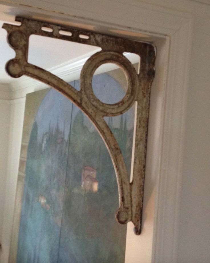 an old mirror hanging on the side of a white wall next to a doorway with a painting behind it