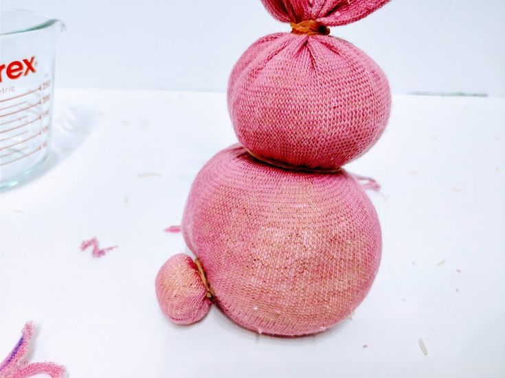 a pink knitted object sitting on top of a table next to a measuring cup