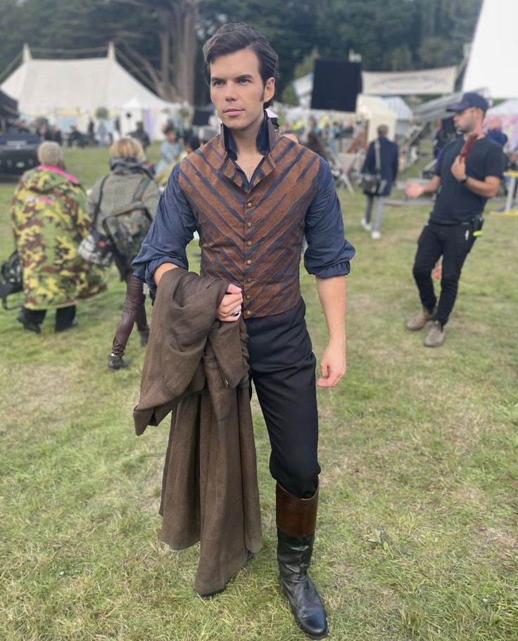 a young man dressed in period clothing at an outdoor music festival with other people around him