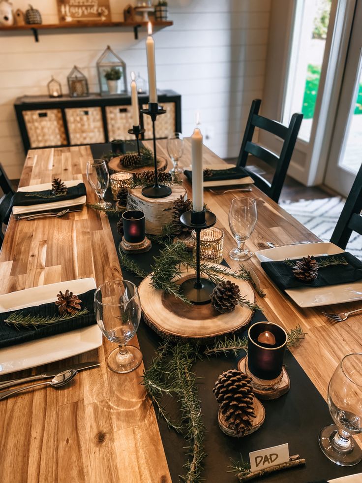 the table is set with pine cones, candles and place settings for two people to sit at