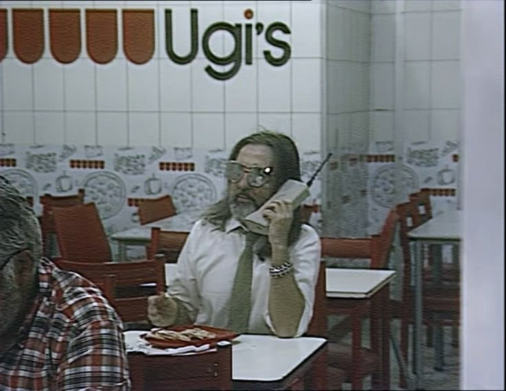 a man sitting at a table talking on a cell phone while holding a knife in his hand