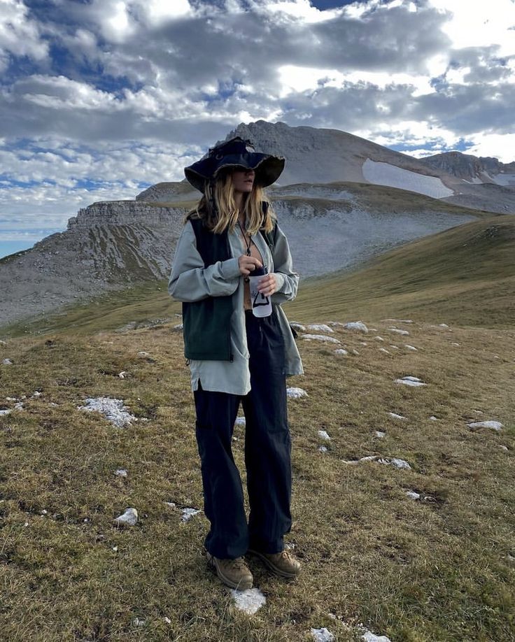 a woman standing on top of a grass covered hillside