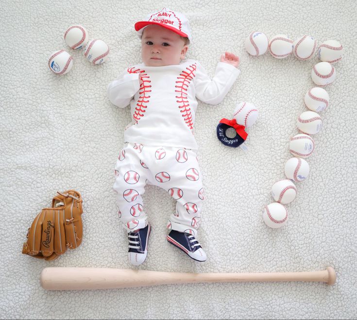 a baby laying on top of a bed next to baseball equipment