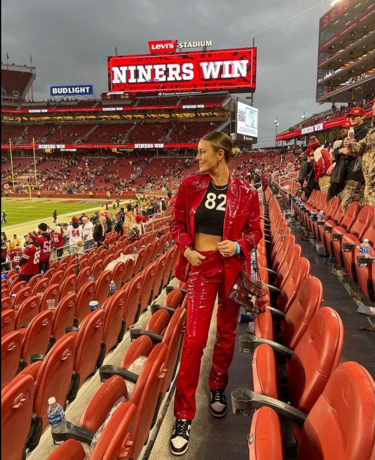 a woman is standing in the bleachers at a baseball game wearing red pants and a black top