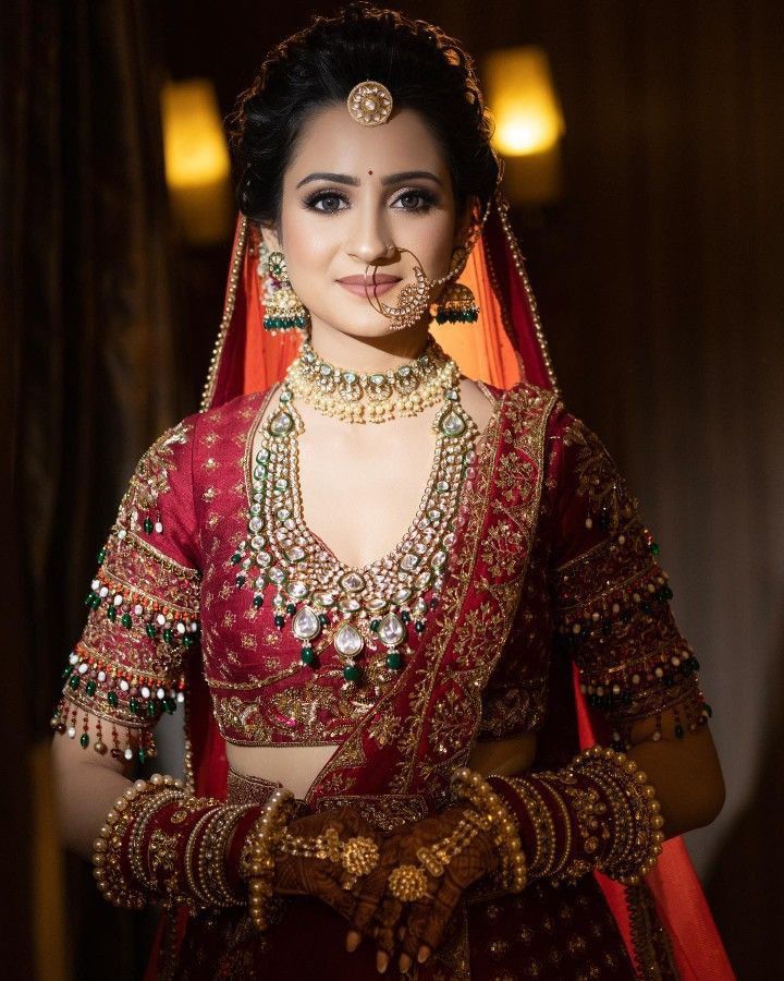 a woman in a red and gold bridal outfit with jewelry on her face, posing for the camera