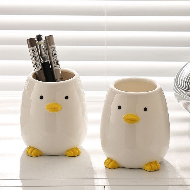 two mugs with pens and pencils in them sitting on a table next to a window