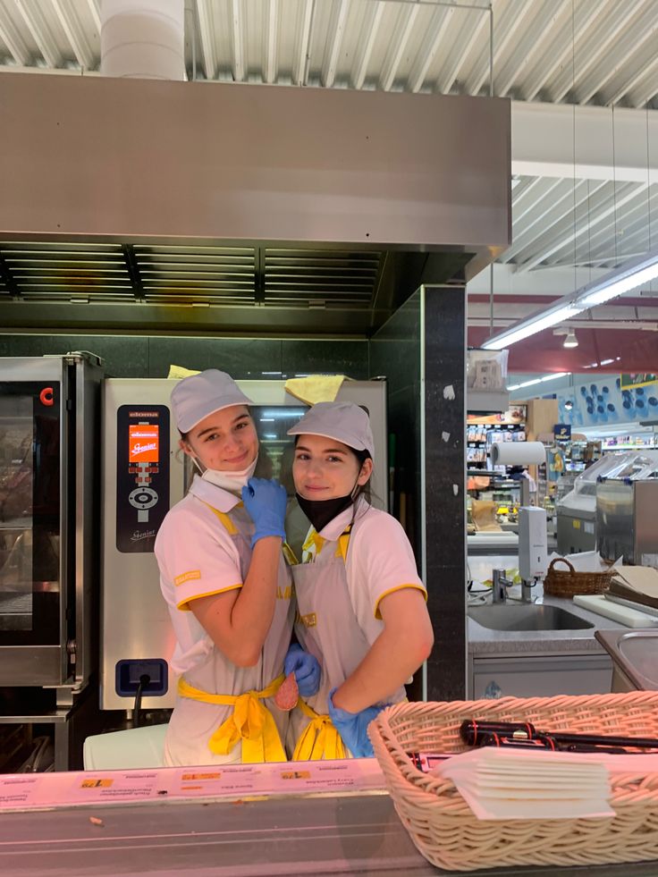 two women in uniforms standing next to each other near a counter with food items on it