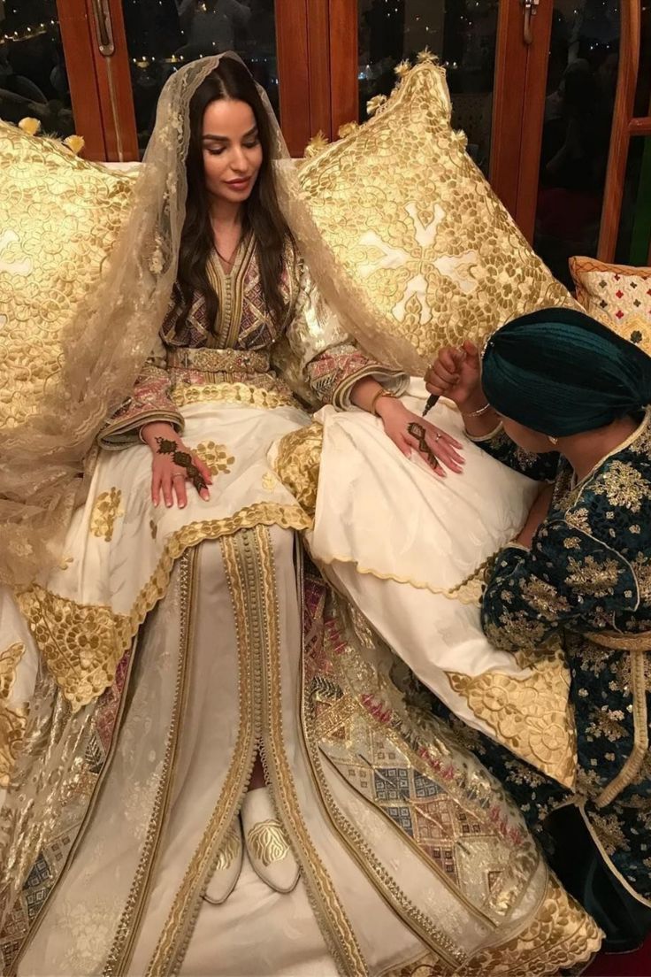 a woman in a wedding dress sitting on a bed next to a man wearing a green turban